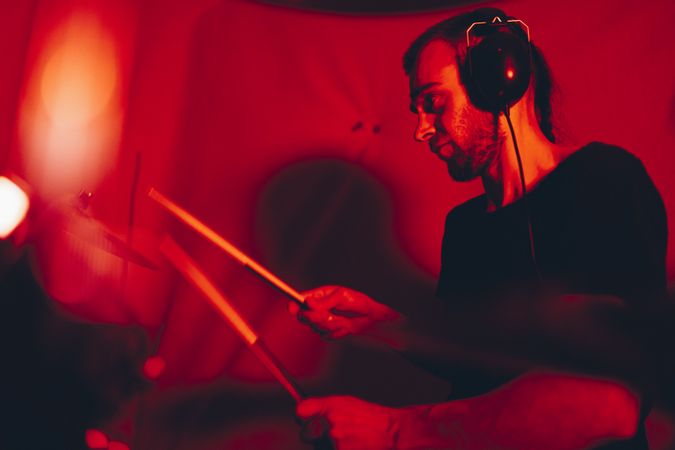 Man with drumsticks playing on drums in redness