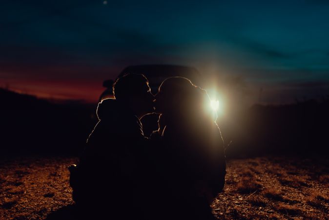 Men hugging and sitting on ground near car on field at night