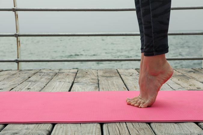Female legs on yoga mat on wooden floor outdoors, space for text