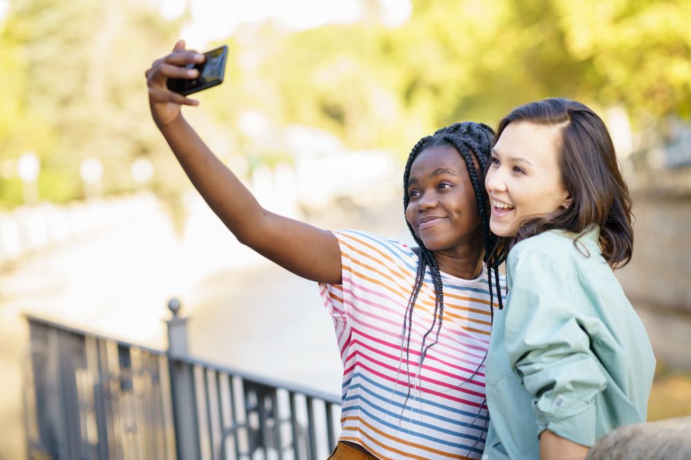 Women friends taking selfie with phone in casual clothing outside
