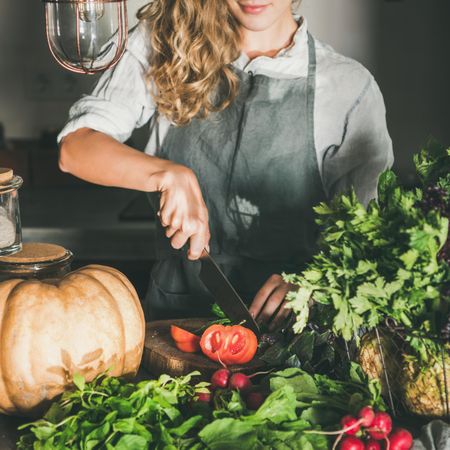 Woman cutting tomato in rustic kitchen, square crop