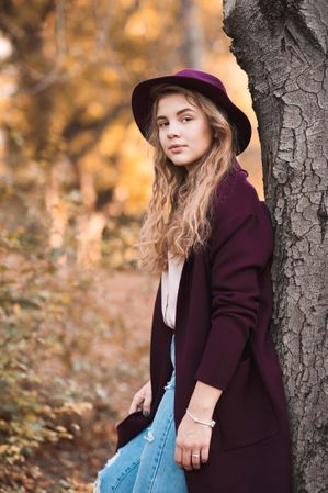Teenage girl in purple coat and hat leaning on tree