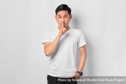Asian male in grey studio making “shhh” sign 5XeaV4