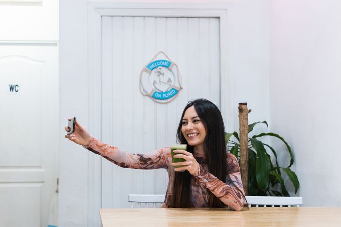Smiling woman taking self portrait on smartphone at table in bar