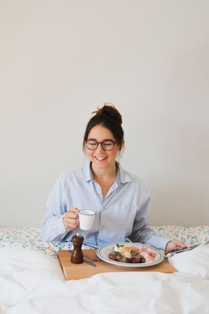 Young woman with breakfast on bed using smart phone