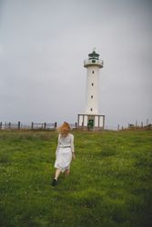 Woman walking in green meadow near lighthouse