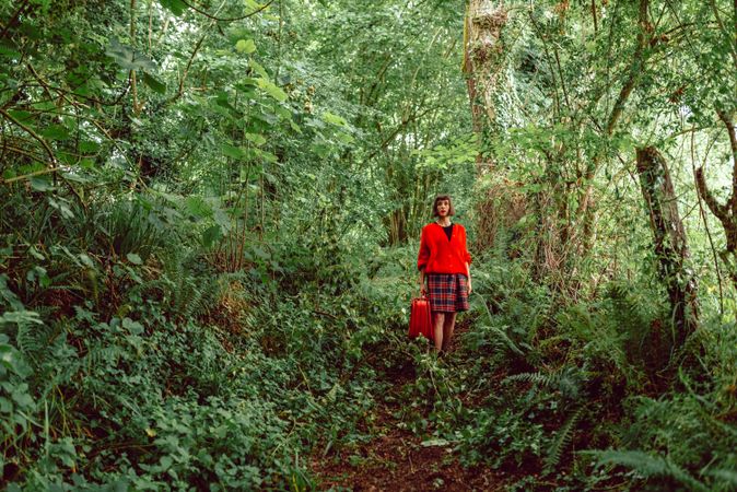 Woman in red with big red suitcase in forest