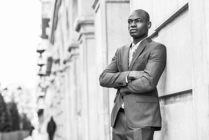 Serious male in business attire leaning on wall with arms closed, B&W