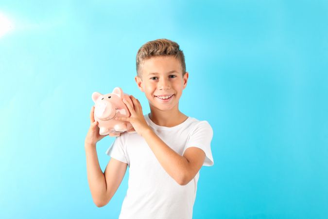 Boy with piggy bank against color background, space for text
