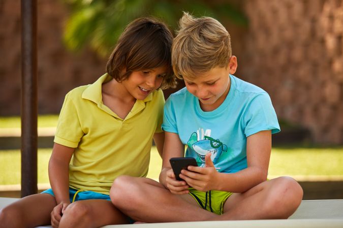 Cheerful boys browsing smartphone on sunbed