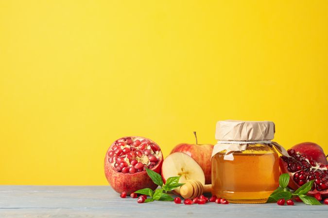 Apples, pomegranate, and honey pot in bright yellow room with copy space