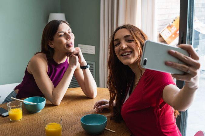 Happy women having lunch and browsing smartphone at home
