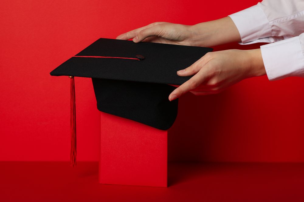 Graduate hat with diploma on red background.