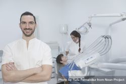 A portrait of a smiling dentist with teenage patient sitting in the background 4ZX730