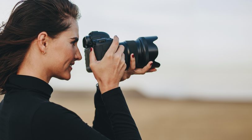 Side view of female photographer shooting with dslr camera outdoors