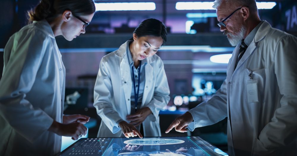 Modern Hospital Medical Research Center: Diverse Colleagues Gathered Around Interactive Touch Screen Table With MRI Scans Of Brain On Display.
