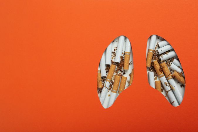 Lung shape cut out of orange paper with cigarettes with copy space
