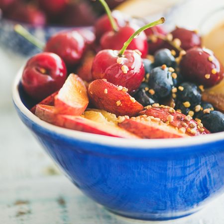 Close up of blue bowl of fresh fruit with cherries, peaches, blueberry, square crop