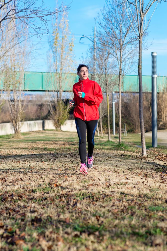Woman in red running outdoors in the grass on sunny fall day