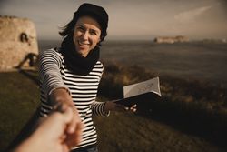 Smiling woman with notebook holding hand on shore near water
