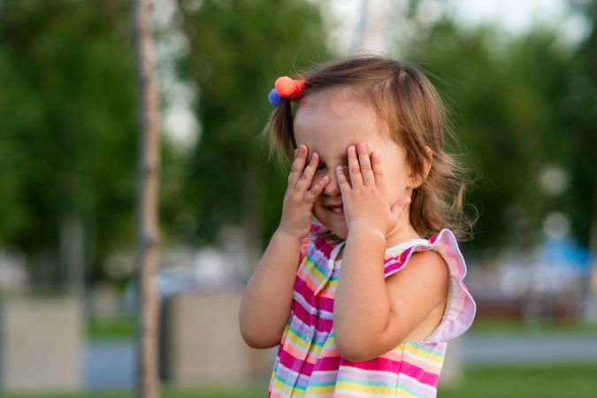 Toddler covering eyes in park outdoors