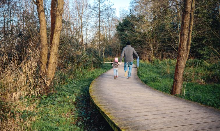 Back of father in fall coats walking with daughter in forest