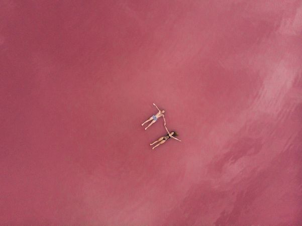 Idyllic couple in swimwear floating in pink water of lake