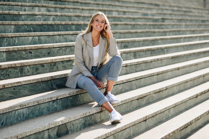 Smiling woman in blazer sitting on outdoor steps on sunny day