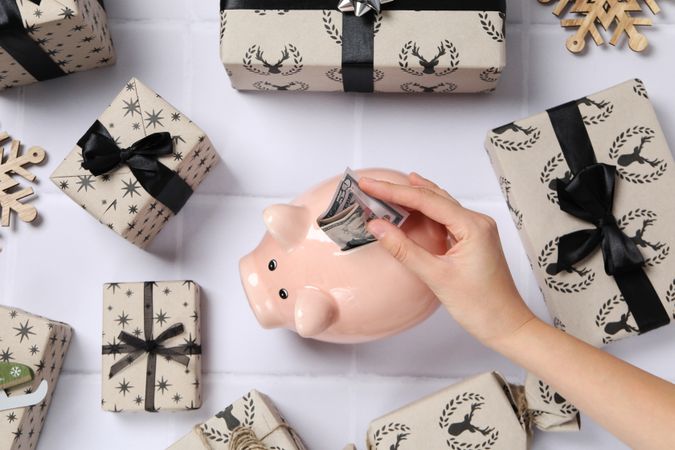 Piggy bank, gift boxes and hand with cash on light background, top view