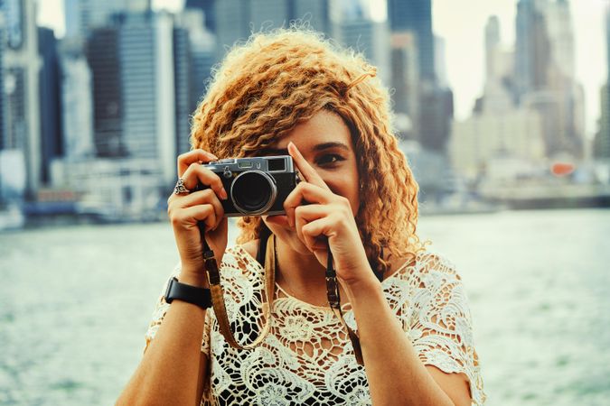Black woman photographer taking photos with Manhattan skyscrapers in the background, close up