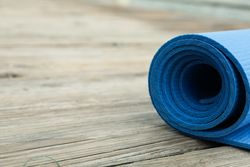 Blue yoga mat on wooden background, space for text