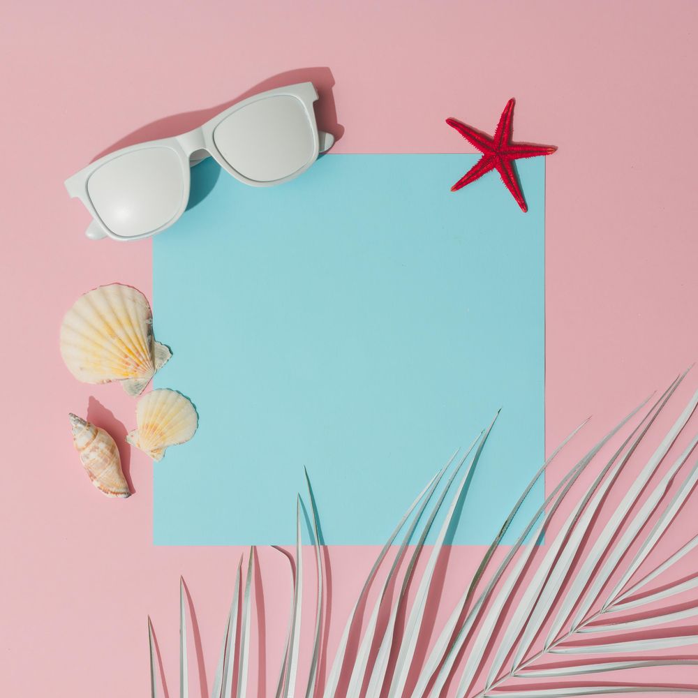 Beach accessories and palm leaves on pastel pink and blue background