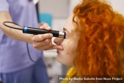 Red haired woman in clinic with medical device checking her eye 4ZZRN4
