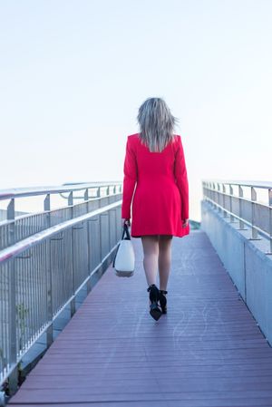Rear shot of woman in red coat walking on foot bridge