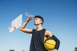 Young man standing with ball and playing on basketball court outdoor.
