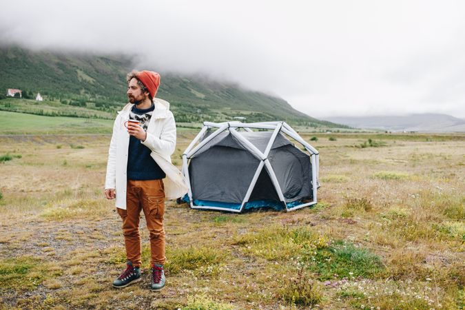 Calm man waking up from tent with ceramic mug on overcast day