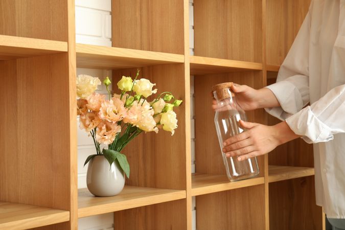 Young woman with bottle near wooden shelves with flowers