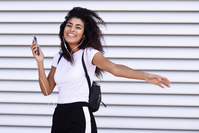 Arab woman in sport clothes with curly hair standing in front of wall with phone