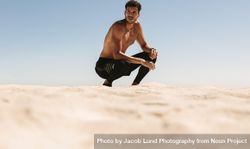 Fit male crouching and looking to the side during workout on seashore 5plex5