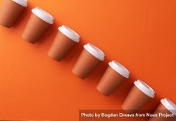 Diagonal row of disposable coffee cups on orange background 4Bg2Mb