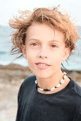 Boy wearing shell necklace looking at camera at beach