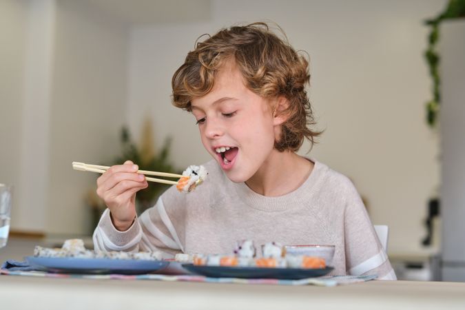Blond child eating sushi at table