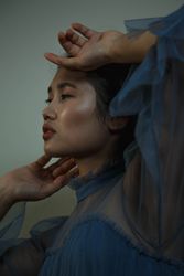 Side view of young woman in blue chiffon top touching her face