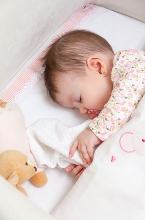 Baby girl sleeping in a cot with pacifier and toy