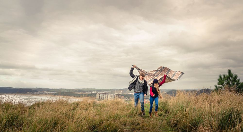Portrait of loving couple playing outdoors with blanket on a windy day over dark cloudy sky