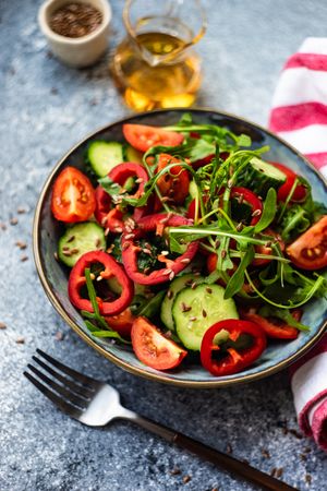 Healthy vegetable salad with organic cucumber, tomatoes, bell pepper, arugula and flax seeds on grey background