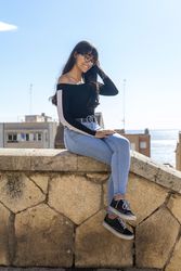 One young woman in eyeglasses sitting on stoned beach wall
