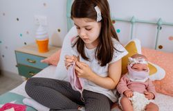 Girl sewing face masks for herself and her baby doll
