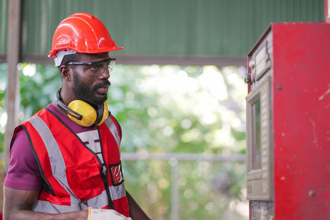 Black male factory worker operating control big machine in the industrial construction