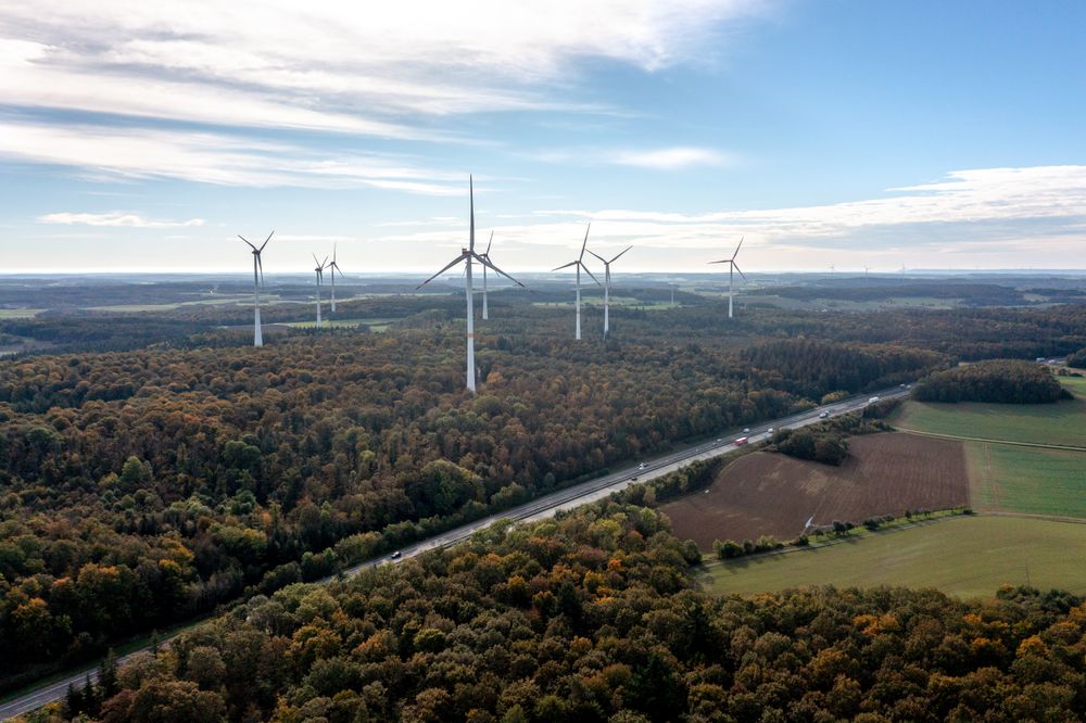 Wind turbines and highway in an autumn forest, drone aerial view